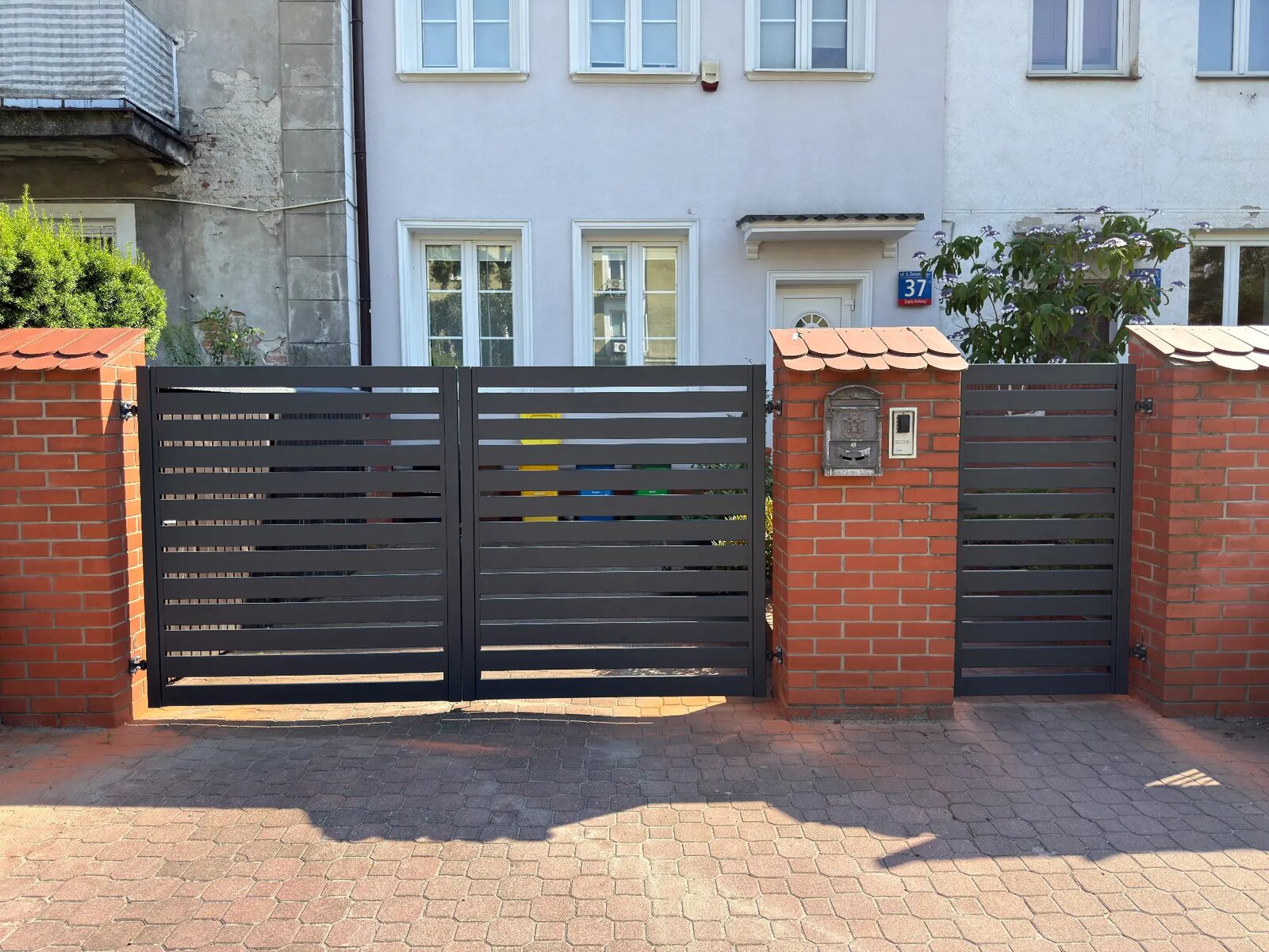 Antracytowa brama i furtka z poziomych profili między ceglanymi słupkami